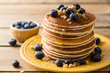Pancakes with blueberries, walnuts and honey on wooden background.