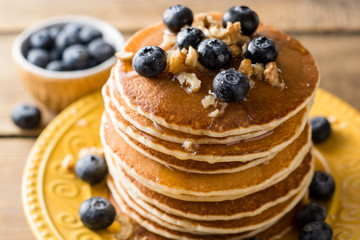 Pancakes with blueberries, walnuts and honey on wooden background.