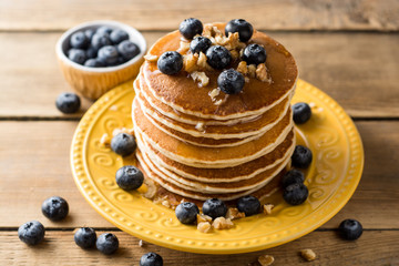 Pancakes with blueberries, walnuts and honey on wooden background.