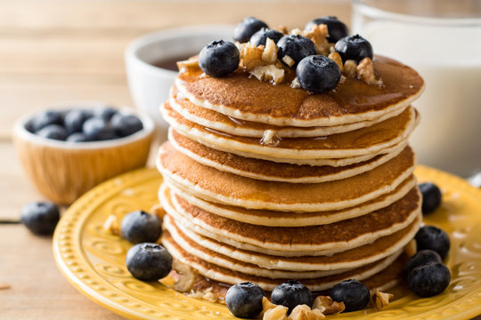 Pancakes with blueberries, walnuts and honey on wooden background.