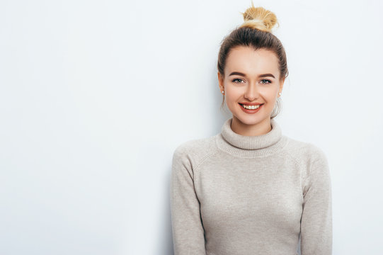 Horizontal portrait of cheerful woman with appealing smile, having hair bun wearing in sweater isolated over white background. Beautiful female showing her pleasant emotions. People Beauty Fashion