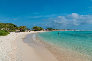 Fototapeta na wymiar tropical Caribbean beach at sunset with straw umbrellas and white sand island of Aruba