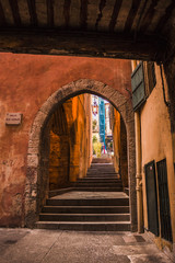 Arches in Villefranche-sur-mer with orange wall in narrow path through the town, France