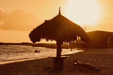 tropical Caribbean beach at sunset with straw umbrellas and white sand island of Aruba