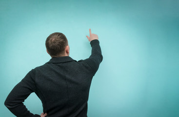 Focused man points a finger at a copy space in front of him and is selecting item from virtual menu isolated on blue background. Back view.