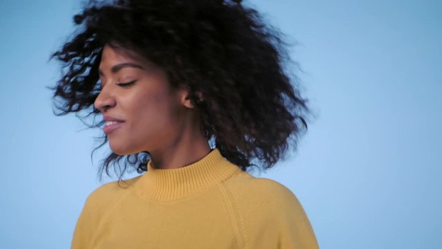beautiful black woman with afro hair having fun smiling and dancing in studio against blue background. slow motion