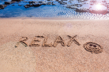In the sand on the beach, the word relax is written. The blue ocean. Gold sand. Summer. Concept. Free space for text. Mock up.