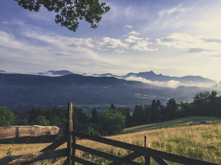 Fototapeta na wymiar Blick über Wiesen und Berge mit einem Holzzaun im Vordergrund