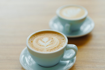 Two cup of coffee  in a beautiful blue cup on a wooden table in a coffee shop. A cappuccino mug with a pattern on the foam. 