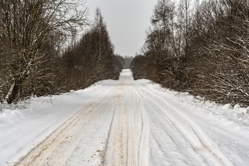 Obraz premium a rural snowy road with snowdrifts on the roadside, tree branches covered with snow caps