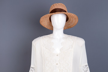 Fashionable straw hat with ribbon. Female mannequin in modern headgear and lace blouse, grey background. Feminine elegant wardrobe.