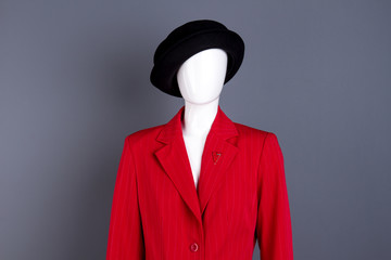 Female mannequin in elegant outfit. Black hat and red blazer on female mannequin, grey background. Ladies fashion style.