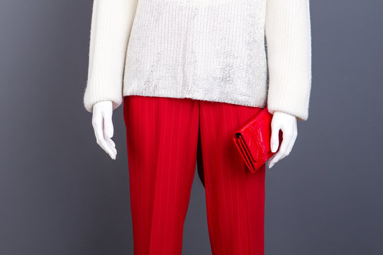 White sweater, red trousers and wallet. Female mannequin dressed in white knit pullover and red trousers, cropped image. Feminine beauty and style.