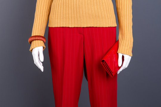 Red trousers, wallet and bracelet. Female mannequin dressed in yellow sweater and red trousers close up, cropped image.