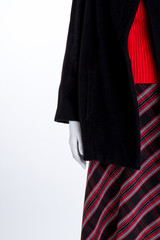 Close up black coat and striped skirt. Female mannequin in red sweater and black overcoat close up, copy space. Boutique of ladies outfit.