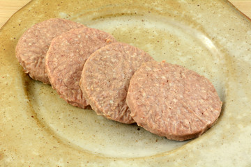 Frozen raw hamburger patties thawing out on ceramic plate as grilling preparation