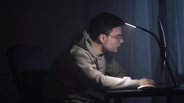 Exhausted young unshaved caucasian man in glasses wakes up in front of computer at night