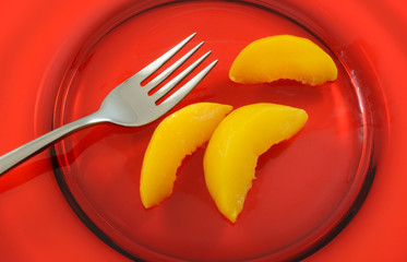 Closeup of canned peach slices on red glass plate for healthy dessert