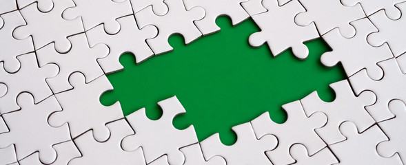 Close-up texture of a white jigsaw puzzle in assembled state with missing elements forming a green...