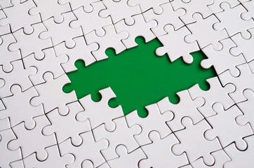 Close-up texture of a white jigsaw puzzle in assembled state with missing elements forming a green...
