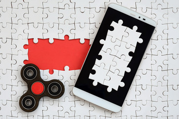 A modern big smartphone with a touch screen and a spinner lie on a white jigsaw puzzle in an...