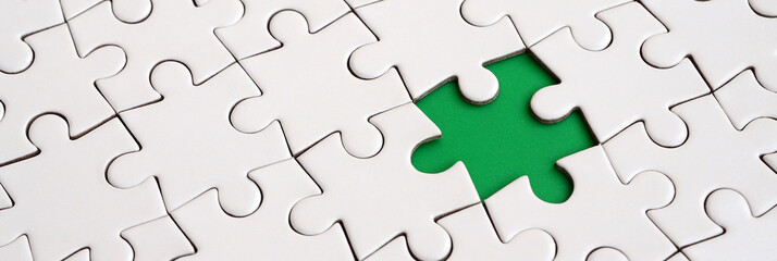 Close-up texture of a white jigsaw puzzle in assembled state with missing elements forming a green...