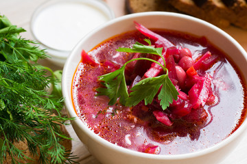 Borscht-vegetable beetroot soup, on the table with slices of rye cereal bread and gluten of sour cream, garlic and herbs. Rustic style.
