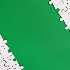 Fragment of a folded white jigsaw puzzle on the background of a green plastic surface. Texture...