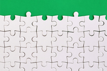 Fragment of a folded white jigsaw puzzle on the background of a green plastic surface. Texture...