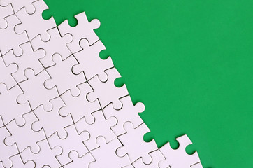 Fragment of a folded white jigsaw puzzle on the background of a green plastic surface. Texture...