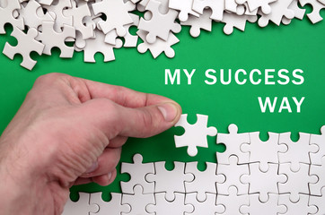 My success way. The hand folds a white jigsaw puzzle and a pile of uncombed puzzle pieces lies...