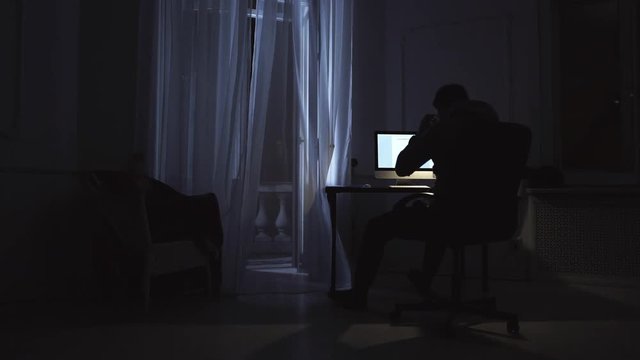 Young man finish work on script on computer at night room, black cat on window sill, curtain shakes on wind