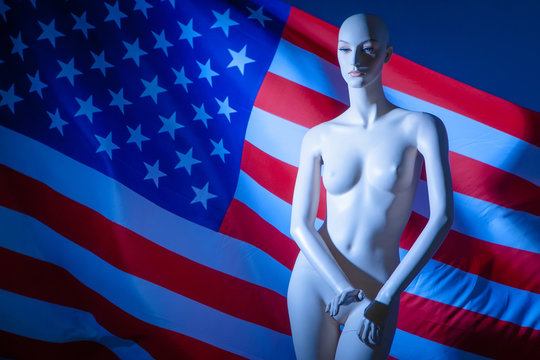 Mannequin for clothes on a background of the flag of the USA. American flag. Naked mannequin woman against the background of the US flag. Sexual harassment.
