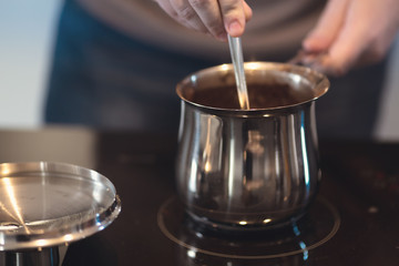 Man preparing turkish black coffee on the kitchen stove in a metal pot