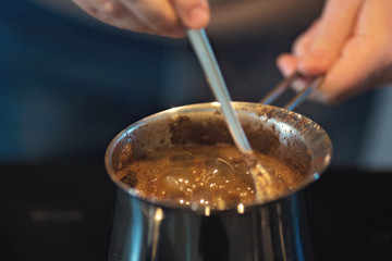 Man preparing turkish black coffee on the kitchen stove in a metal pot