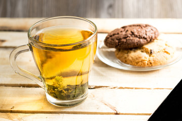 Transparent cup with herbal tea and an American chocolate chip cookie on a transparent plate on a wooden table