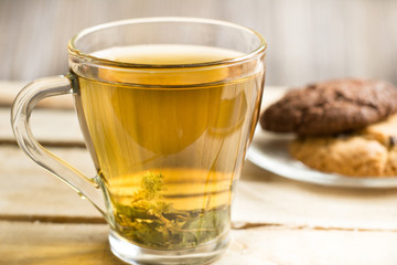 Transparent cup with herbal tea and an American chocolate chip cookie on a transparent plate on a wooden table