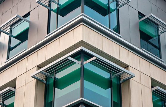 Corner of a modern building with green glass, stone facade, and aluminum awnings.