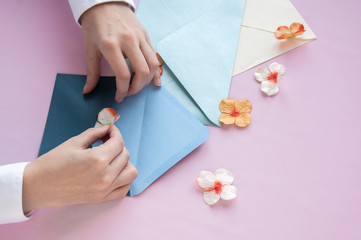 Female hands put the flower in a blue envelope on a pink background