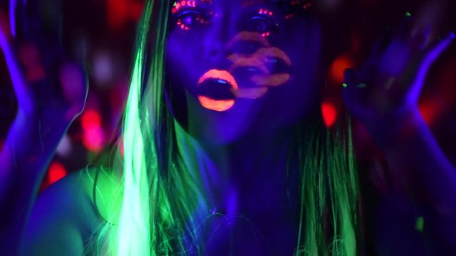 Fashion model girl with colorful fluorescent makeup in neon lights. Female disco dancer in UV light. Night club, party. 4K UHD video footage. 3840X2160