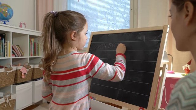 Early childhood development. Young mother explaining arithmetic to cute little daughter with blackboard at home. Play and learn. Slow motion