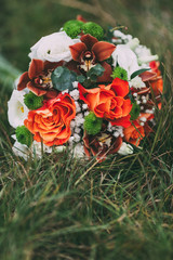 Wedding bouquet of orange and cream roses on green grass. Side view. Artwork