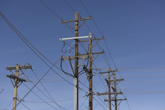 Row of wooden telephone or utility poles and power lines against a clear blue sky. With Copy Space
