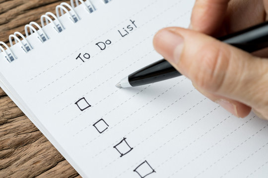 To do lists, finish work, tasks priority concept, closed up of hand holding pen writing list on white paper notepad on wood table in soft tone