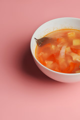Hot vegetable soup with chicken meat in a bowl. a leaf of greenery. on a pink background. The concept of a healthy food and diet