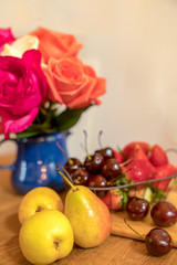 Fruits plate on the table with many roses in blue vase . Selective focus on pear and cherry in the front