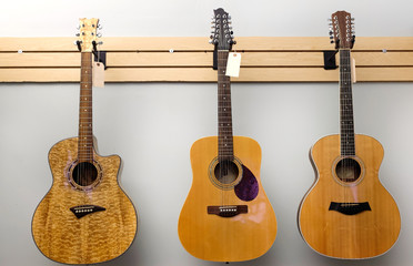 Three acoustic guitars for sale hanging on wall.