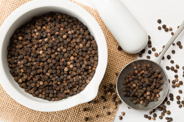 Raw, natural, unprocessed black pepper peppercorns in mortar and metal spoon