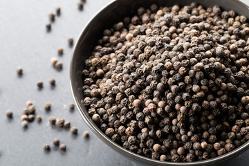 Raw, natural, unprocessed black pepper peppercorns in black bowl