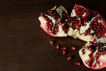 Cut open pomegranate with scattered pomegranate seeds on dark timber background - with copy space